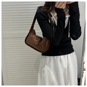 Detailed close-up of brown glossy leather shoulder bag with fashion lettering on the flap
