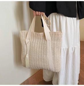 Détail du sac cabas en paille beige avec anses tissées et pompon décoratif porté