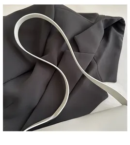 Detail of a white leather shoulder bag featuring a thick, rounded strap on a black blazer