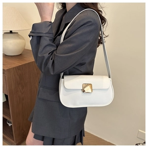 Close-up of a cream shoulder bag with a large gold buckle on a model in a modern interior