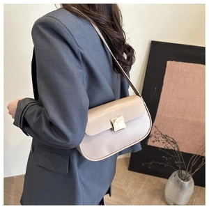 Detail of minimalist beige saddle shoulder bag with gold buckle on a gray blazer model