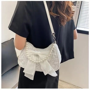 Detailed close-up of white pleated fabric shoulder bag with satin bow and pearl chain