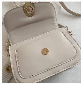 Close-up of the beige saddle bag showing the gold magnetic buckle and front pocket detail