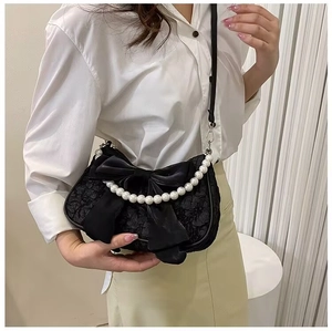 Detail of black bow hobo bag featuring premium pleated fabric and white pearl handle strap