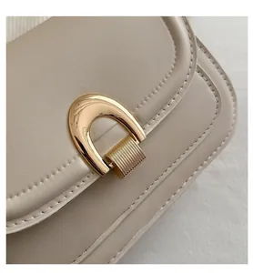 Detailed close-up of golden U-shaped metal buckle on cream faux leather shoulder bag