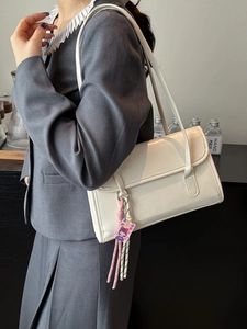 Creamy rectangular underarm bag with long straps and charm shown with a grey blazer