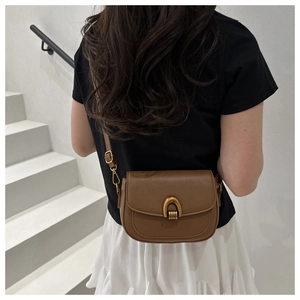 Sac besace en cuir marron avec boucle fer à cheval dorée porté par un mannequin