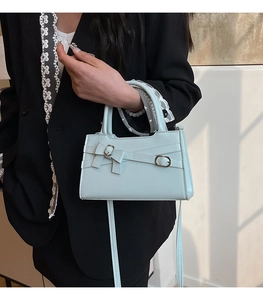Close-up of light blue handbag with bow detail and silver metal buckle on a dark background