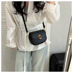 Détail du sac besace en cuir noir minimaliste avec boucle fer à cheval dorée et bandoulière