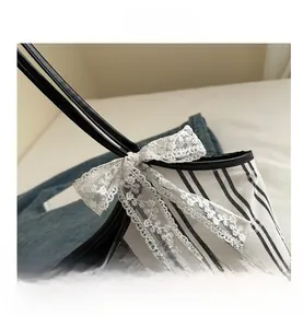 Close-up of white lace bow on striped canvas tote bag with black leather trim detail