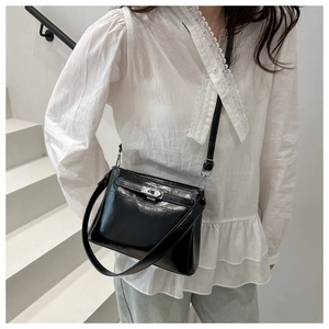 Detailed close-up of a black glossy handbag with a metallic turn-lock and adjustable strap