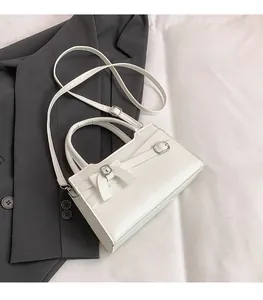 Detail of white handbag with bow decoration and adjustable strap on a grey suit
