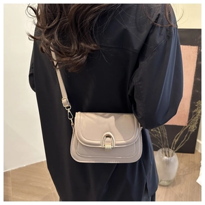 Detail of a minimalist beige square crossbody bag with a golden horseshoe lock buckle