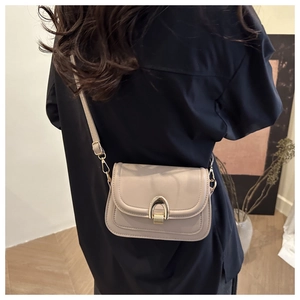 Close-up of cream square shoulder bag with gold U-shaped lock on a black shirt