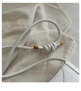 Detail of white leather shoulder strap with handcrafted knot and gold metal tips