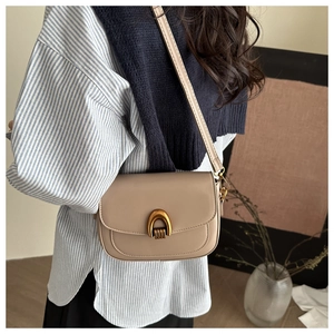 Détail du sac de selle beige avec boucle dorée en forme de U porté par un mannequin