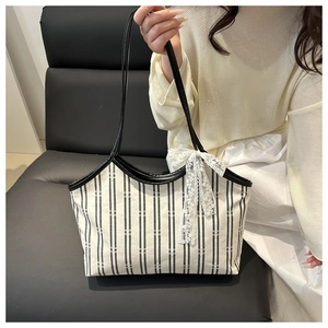 Detail of canvas tote bag featuring black stripes and a delicate white lace bow accent
