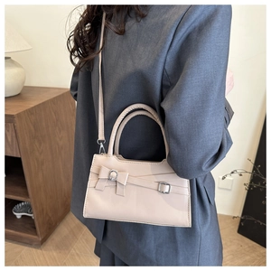 Detail of beige structured handbag with bow decor and silver buckle on grey blazer
