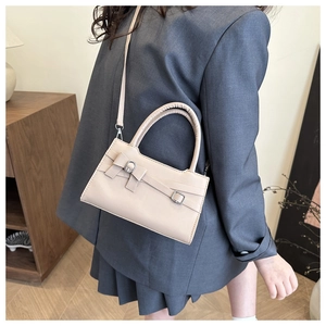 Close-up of beige crossbody bag featuring leather bow detail and silver buckles on model