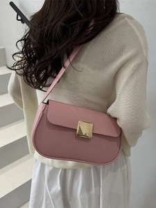 Pink leather shoulder bag with gold buckle on model in minimalist indoor setting