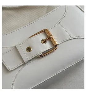 Detailed close-up of golden metal buckle and stitching on creamy white leather bag