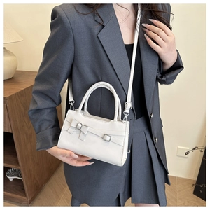 Close-up of white leather handbag featuring ribbon bow and elegant silver buckle detail