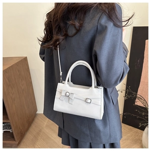 Close-up of white glossy patent leather crossbody bag with bow detail on a model