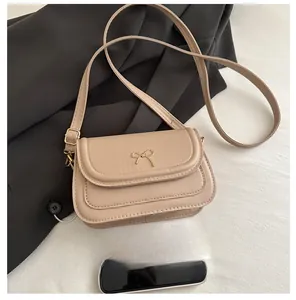 Detail of beige crossbody bag with golden bow buckle and adjustable strap