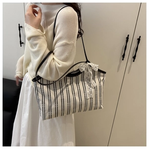 Detail of a striped canvas tote bag with a white lace bow accent on a female model