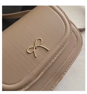 Detail of elegant beige leather bag featuring a golden bow-shaped lock and stitching