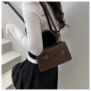 Close-up of brown faux leather handbag with ribbon detail and silver buckles on stairs