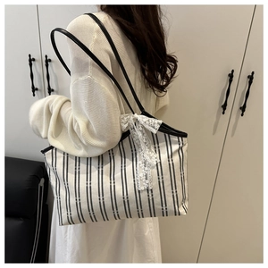 Detailed view of striped canvas tote bag with a white lace bow on model shoulder