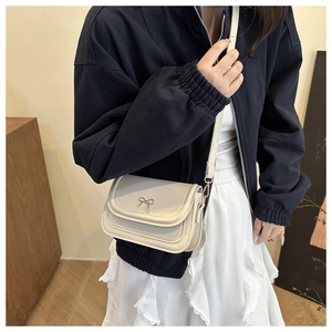 Detail of a creamy white leather crossbody bag featuring a golden metal bow fastener
