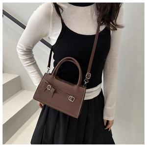 Brown crossbody bag with bow detail worn by a model in a minimalist indoor setting
