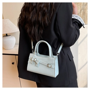 Detailed view of a light blue minimalist crossbody bag styled over a black blazer