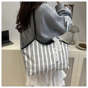Detail of canvas tote bag featuring black and white vertical stripes and lace bow charm