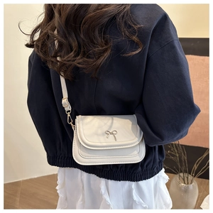 Detail of a creamy white crossbody bag with a silver bow clasp on a navy sweatshirt