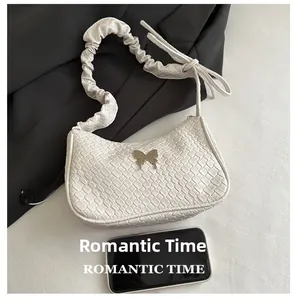 Detailed view of woven leather texture and metal butterfly buckle on white underarm bag