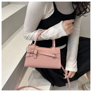 Detail view of a pink leather crossbody bag with bow decoration and silver buckle accents