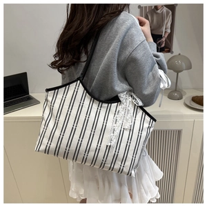 Detailed view of striped canvas tote bag with elegant white lace bow decoration