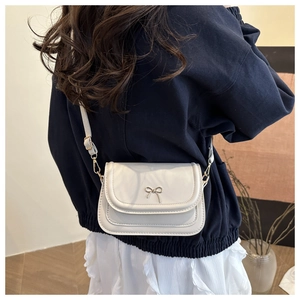 Detail of white leather crossbody bag showing silver bow ornament and metal hooks