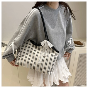 Detail showing elegant white lace bow on beige striped canvas tote bag for women