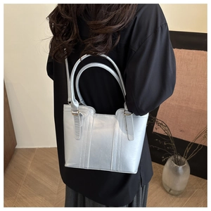 Detail of silver tote bag with vertical stitching and slim shoulder strap on model