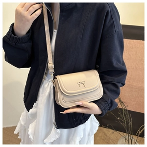 Detail of a cream-colored crossbody bag featuring a golden bow-knot metal clasp and strap
