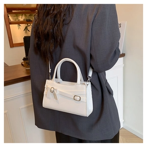 Close-up of white crossbody bag with elegant bow detail and gold hardware on a model