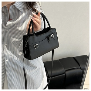 Detail of black crossbody bag featuring a silver square buckle and bow strap detail