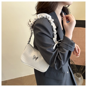 Detail of cream woven shoulder bag with silver butterfly charm and pleated strap