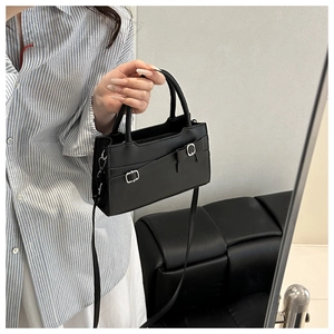 Detail of black mini handbag featuring a matte faux leather finish and metallic buckle bow