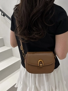 Sacoche selle en cuir marron avec fermoir en U doré porté par un mannequin