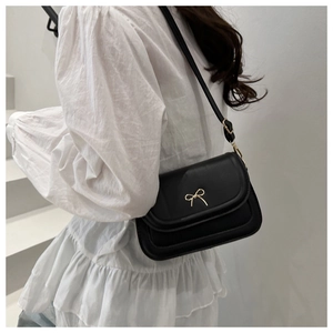 Detail of a black leather crossbody bag featuring a decorative gold bow buckle on the flap